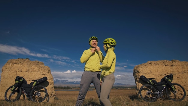 The man and woman travel on mixed terrain cycle touring with bikepacking The two people journey with bicycle bags Mountain snow capped stone arch