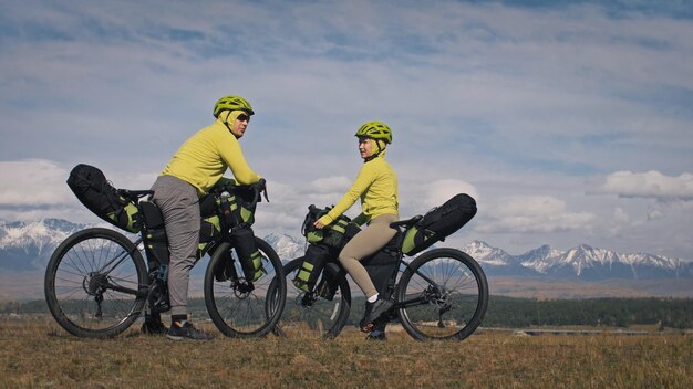 The man and woman travel on mixed terrain cycle touring with bikepacking The two people journey with bicycle bags Mountain snow capped