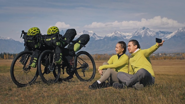 男と女はバイクパッキングで混合地形サイクルを旅します二人は自転車バッグで旅します緑の黒い色のスポーツバイクパッキングバイクスポーツウェア山の雪をかぶった