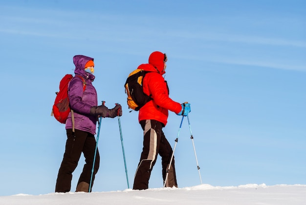 Man and woman travelers go in the winter in the snow against the sky