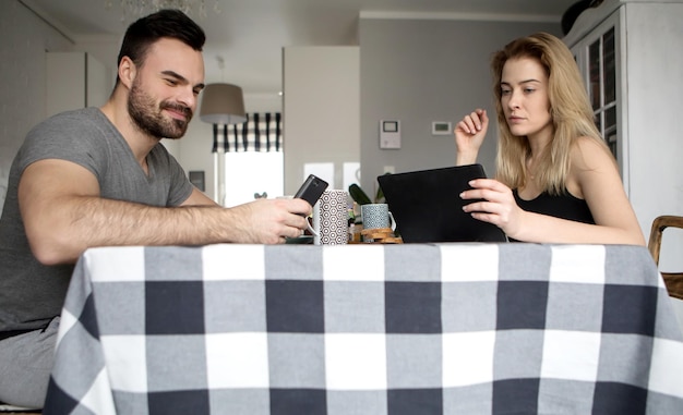 Photo man and woman using technological equipment on dining table at home