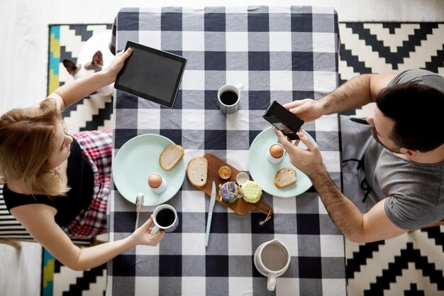 Photo man and woman using technological equipment on dining table at home