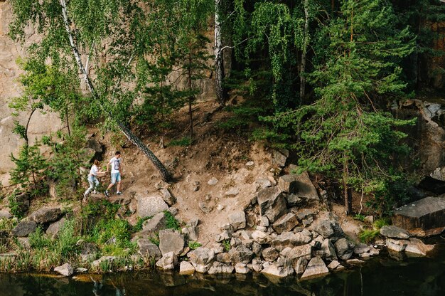 A man and a woman walk along the rocks near the forest and the lake