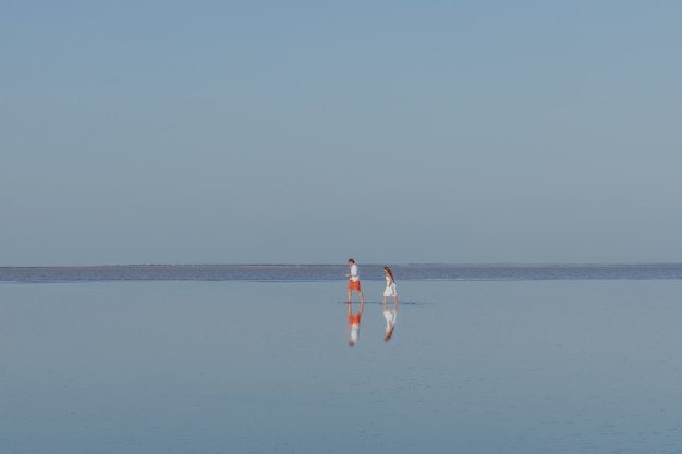 A man and a woman walk on the smooth water of the lake