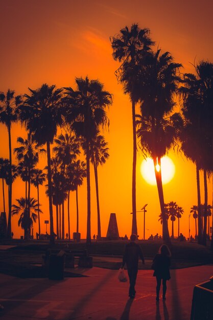 Man and woman walking on footpath against orange sky