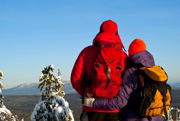 man and a woman in warm sports clothes with backpacks stand their back to the viewer
