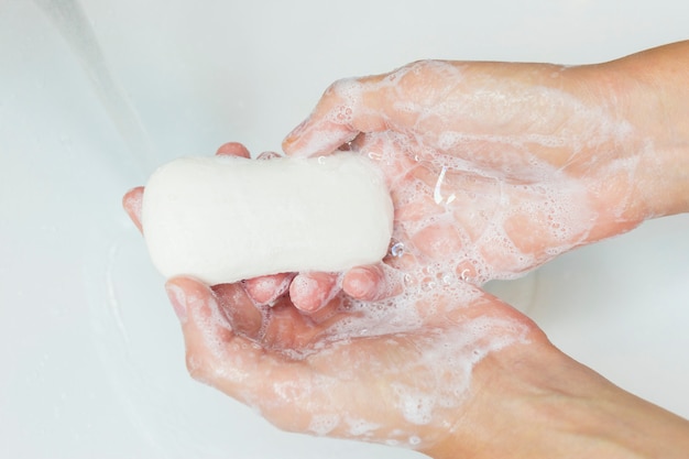 Man or woman washing hands, rubbing with soap in sink under water.