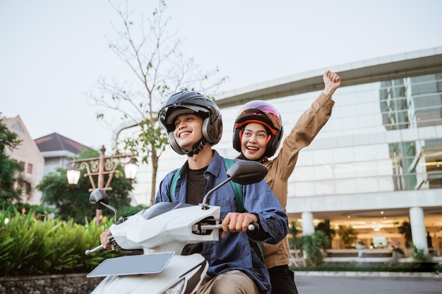 a man and woman wearing helmets with their hands raised while riding a motorcycle