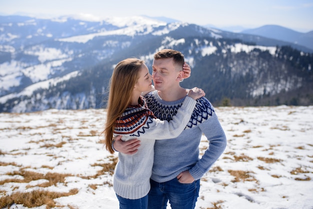 Uomo e donna che indossano abbigliamento tricottato che abbraccia sulla montagna nevosa.