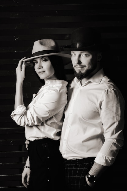 黒の背景に白いシャツと帽子の男と女。愛のカップルがスタジオのインテリアでポーズをとる。黒と白の写真