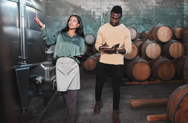 Photo man woman and winemaker giving tour to new employee learning logistics in a winery or wood barrel distillery business owner or ceo working at alcohol manufacturing and vineyard startup warehouse