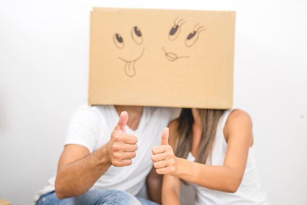 The man and woman with a carton box on the heads thumb up