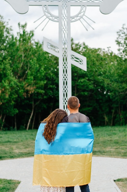 Photo a man and a woman with the flag of ukraine are standing near the cross