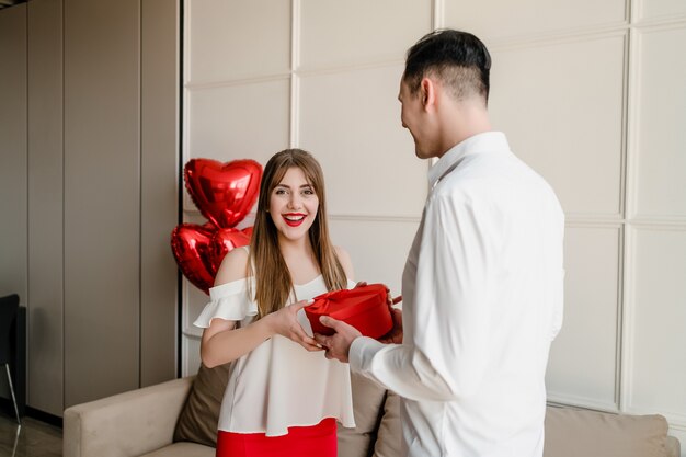 Man and woman with heart shaped gift box and red balloons at home