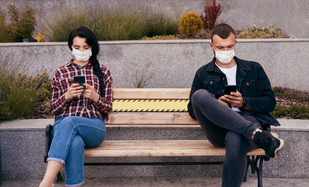 Man and woman with smartphones sitting on bench during pandemic