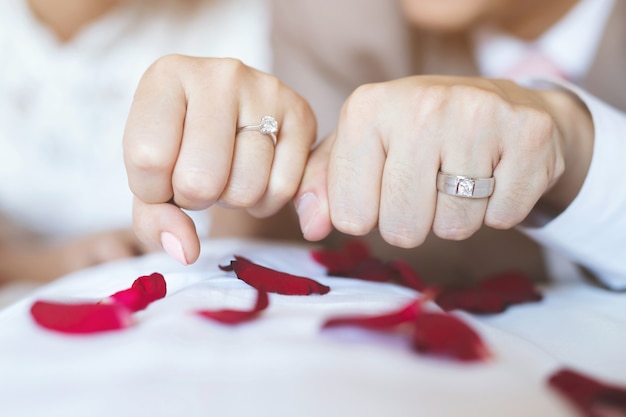 結婚指輪を持つ男性と女性。手をつないでいる若い夫婦、式典の結婚式の日。新婚カップルの手を結婚指輪で。