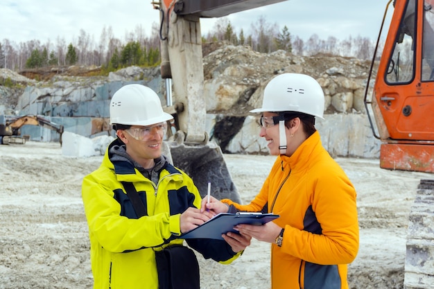 Photo a man and a woman workers in helmets sign a document against the background of construction equipment in a quarry