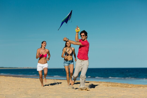 Uomo e donne che corrono sulla spiaggia con l'aquilone