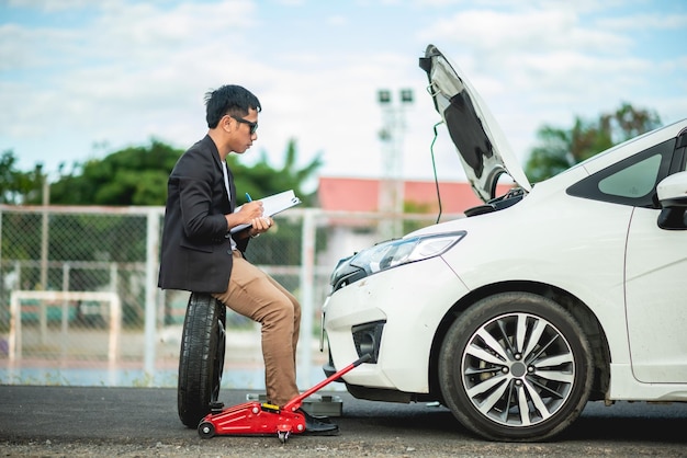 仕事着の男性が自分の車をチェックして、車が壊れているかどうかを確認しています。自動車保険のコンセプト