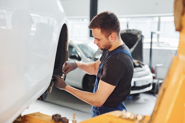 Man in work uniform repairs car indoors conception of\
automobile service