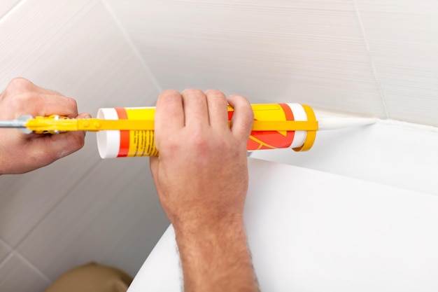 Man worker in bathroom applying sealant