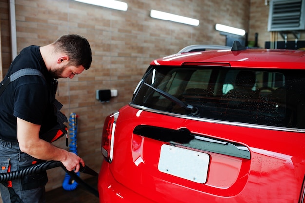 Man worker drying red car in detailing garage after washing