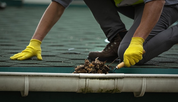 Un lavoratore sta pulendo una grondaia del tetto intasata dallo sporco,