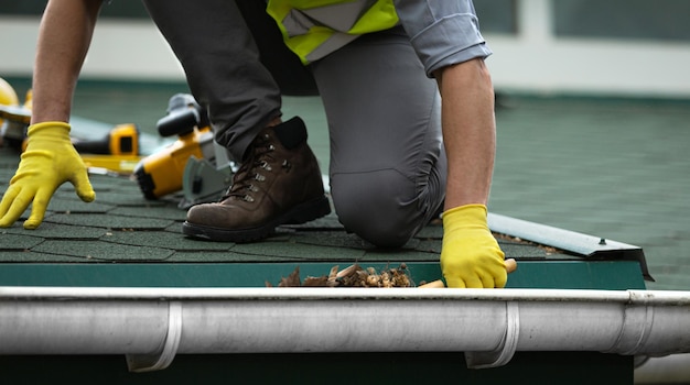 A man worker is cleaning a clogged roof gutter from dirt,