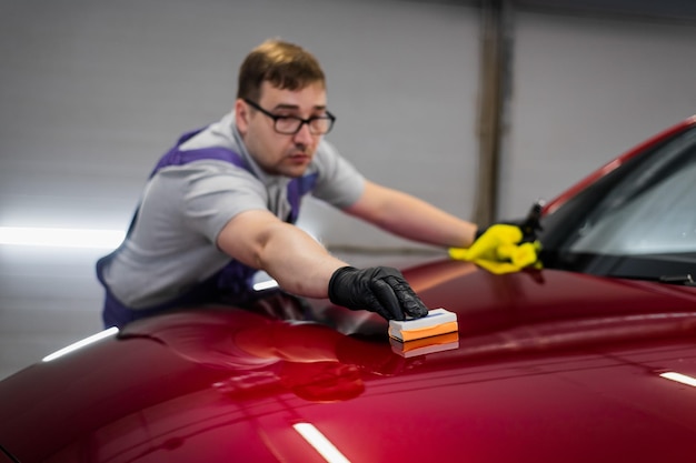 Фото Мужчина, работающий в автомобильной студии, наносит керамическое покрытие на автомобильную краску с помощью губчатого аппликатора