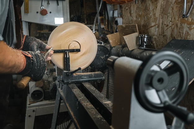 Photo a man in a working apron works on a wood turning lathe hands hold a chisel hobby