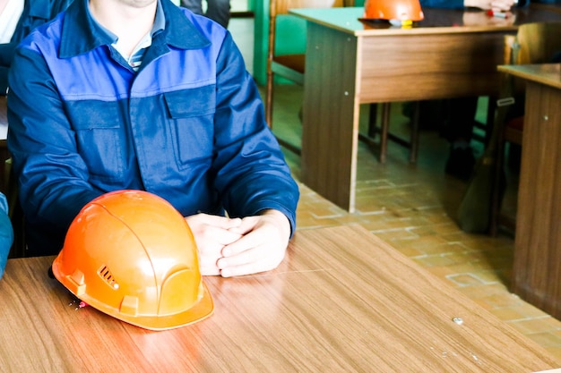 탁자 위에 주황색 노란색 헬멧을 쓴 엔지니어로 일하는 남자가 글쓰기를 공부하고 있다