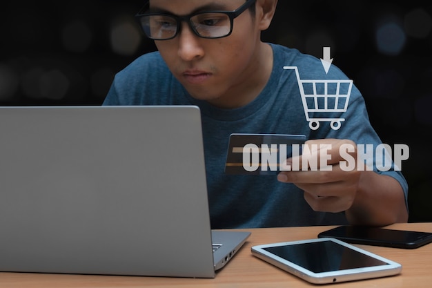 책상 위에 태블릿과 스마트폰이 있는 신용카드를 들고 컴퓨터 노트북으로 책상에서 일하는 남자. 온라인 쇼핑으로서의 소셜 미디어의 개념.
