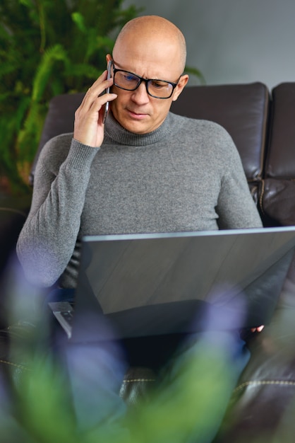 Man working on a blank laptop on a comfortable sofa at home.