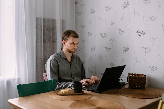 Фото Человек, работающий на ноутбуке за кухонным столом, работает из дома
