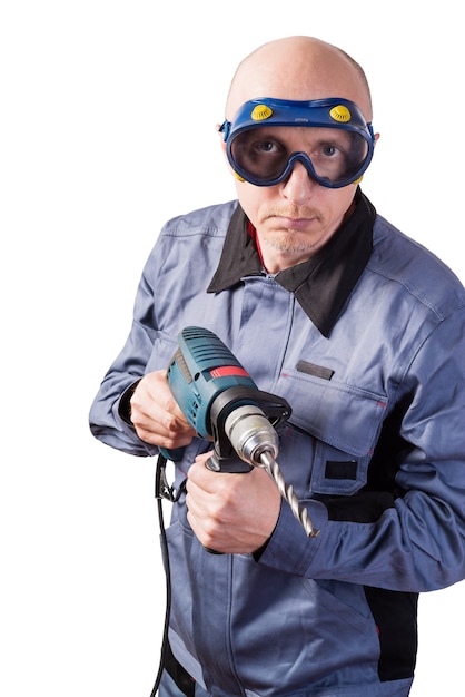 A man in working clothes in goggles with an electric drill