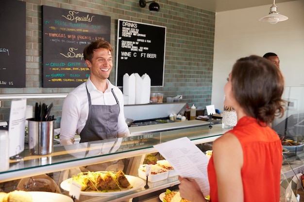 Man Working Behind Counter In Delicatessen Taking Food Order