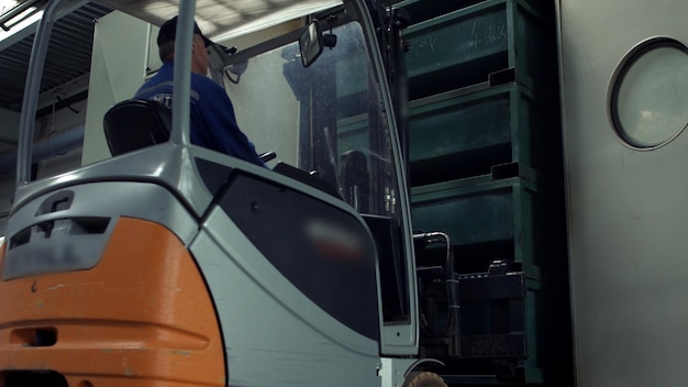 Man working on electric forklift taking away boxes from shelving in warehouse