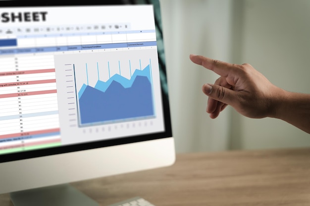 Man working on excel person pointing at computer screen displaying spreadsheet and line graph analyzing data and trends in professional setting