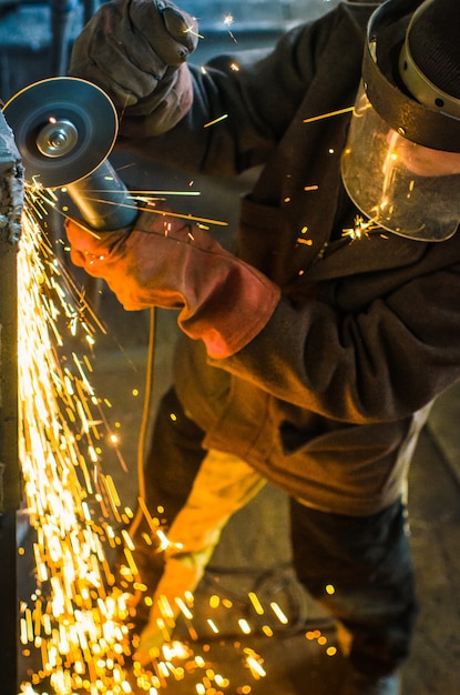 A man in working form and a face mask cuts a metal saw with a Bulgarian