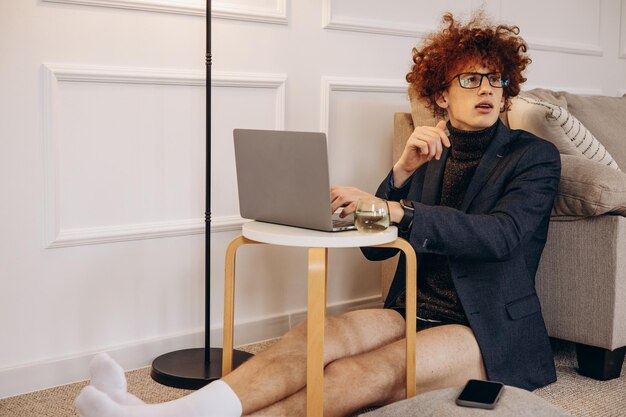 Man working from home on laptop and sitting by the sofa in jacket and underwear