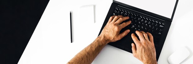 The man working at home on the remote A black-and-white workplace with a laptop alarm clock notebook and mens hands