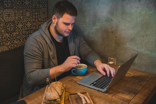 カフェでラップトップに取り組んでいる男。朝食サンドイッチとコーヒーのコンセプト