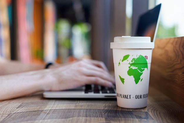 Man working on laptop and drinking from a reusable cup of coffee