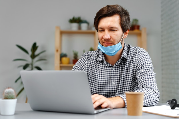 Man working on laptop at home and wearing medical mask