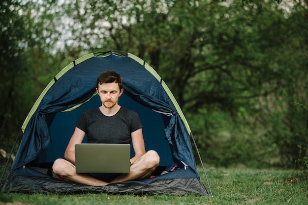 Man working on laptop in tent in forest, meadow