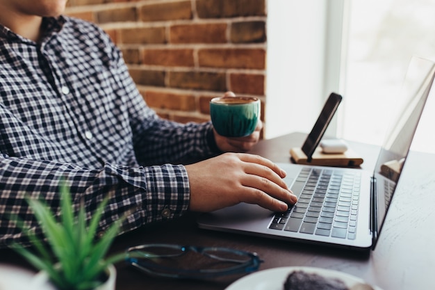 Photo man working at the laptop with a cup of coffee at home. blurred background.