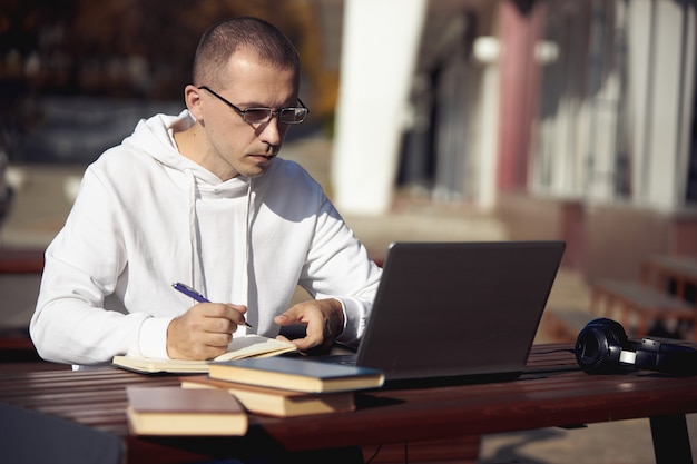 Man working on a laptop and writing in a notebook