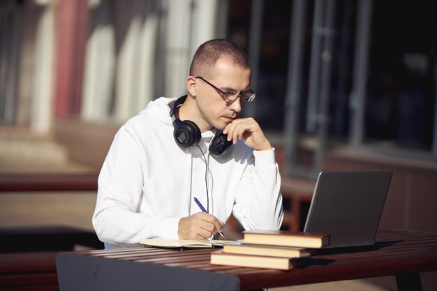 Человек, работающий на ноутбуке и писать в записной книжке, сидя на улице за столом. социальное дистанцирование во время коронавируса
