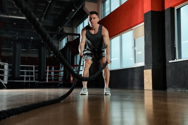 Man working out with battle ropes in modern gym