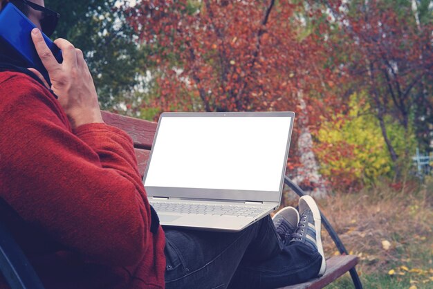 L'uomo che lavora all'aperto è sempre connesso con il suo smartphone e il suo fedele laptop giovane freelance che lavora all'aperto in autunno park